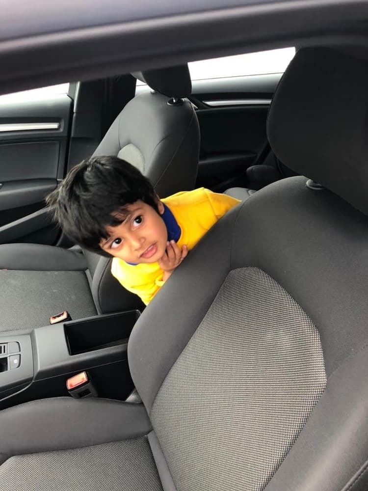 Young Vyom peeking playfully through car seats with curious and attentive eyes